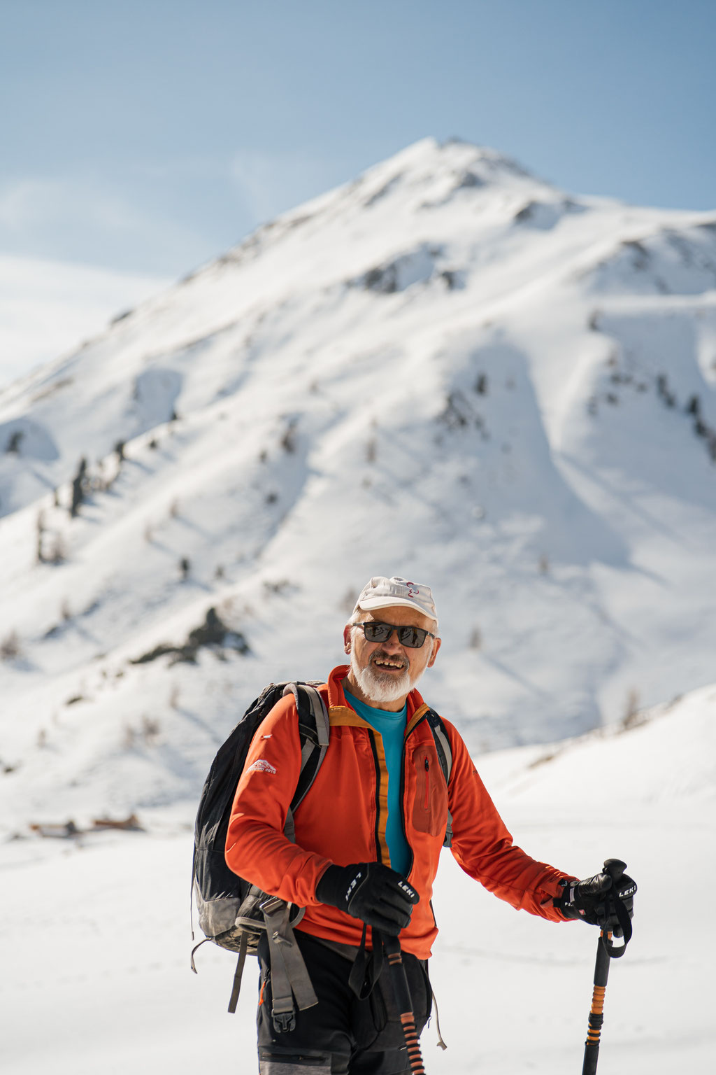 Älterer Wanderer mit Rucksack in verschneiter Berglandschaft.