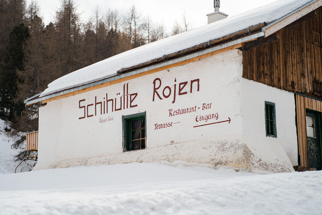 A snow-covered mountain hut with the sign ‘Schihütte Rojen’.