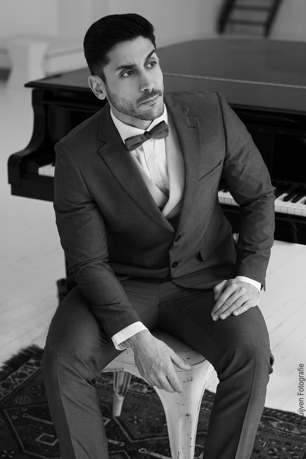 Vasilis gefotografeerd tijdens de Fotoshoot Dag op vrijdag 27 februari 2026 in Studio Duinlust. Vasilis draagt op de foto een mooi groen pak, zit bij een piano op een stoel in de daglichtstudio. Foto is gemaakt door Stefan van Ruijven Fotografie