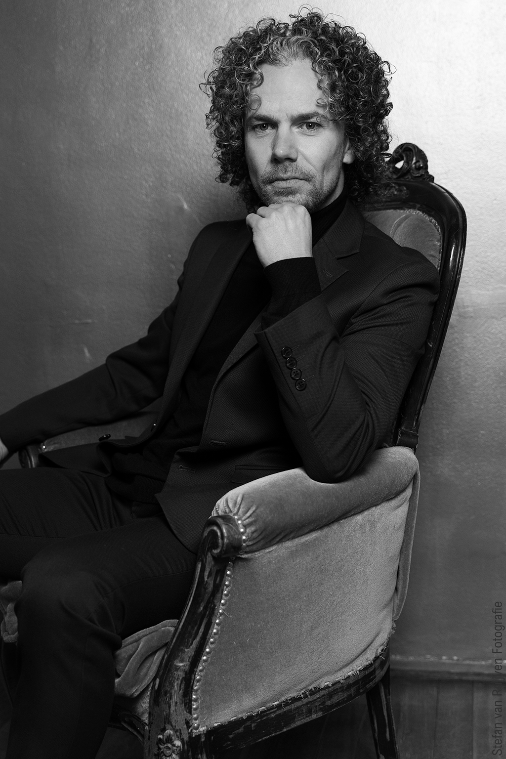 Stefan poseert in kamer met vintage kleed en stoel in Studio Duinlust. Portfolio maken tijdens de Fotoshoot Dag op vrijdag 27 februari 2026. Hij draagt een groen/blauw pak en zwarte coltrui. Foto's gemaakt door Stefan van Ruijven