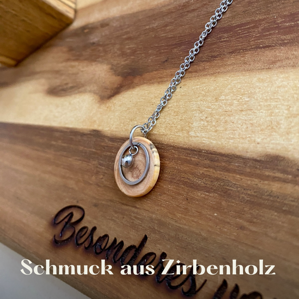 Eine Kette aus Zirpen Holz mit einem kleinen Anhänger liegt auf einem Holzbrett.