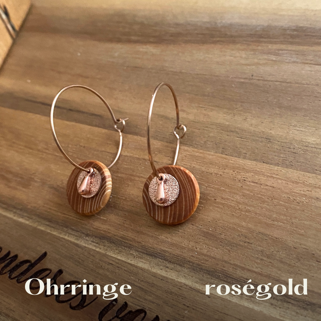 Ohrringe mit Holz und Roségold farbenem Edelstahl liegen auf einem Holzbrett