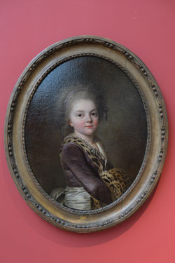 Portrait of young girl, presumed to be of Émilie Charton, 1781. Musee des Beaux-Arts Nancy. Photo: Epochs of Fashion. An oval oil portrait in gold frame showing the torso of a young lady wearing a purple dress with white sash and leopard trim. 