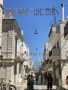 luminarie con canzone volare oh oh, cantare oh oh su strada pedonale e case bianche con gente che passeggia