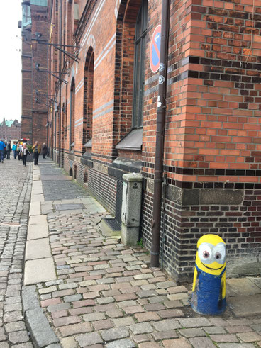 angolo di una strada di Amburgo con palazzo dai mattoni rossi e pilone di cemento colorato come un minions