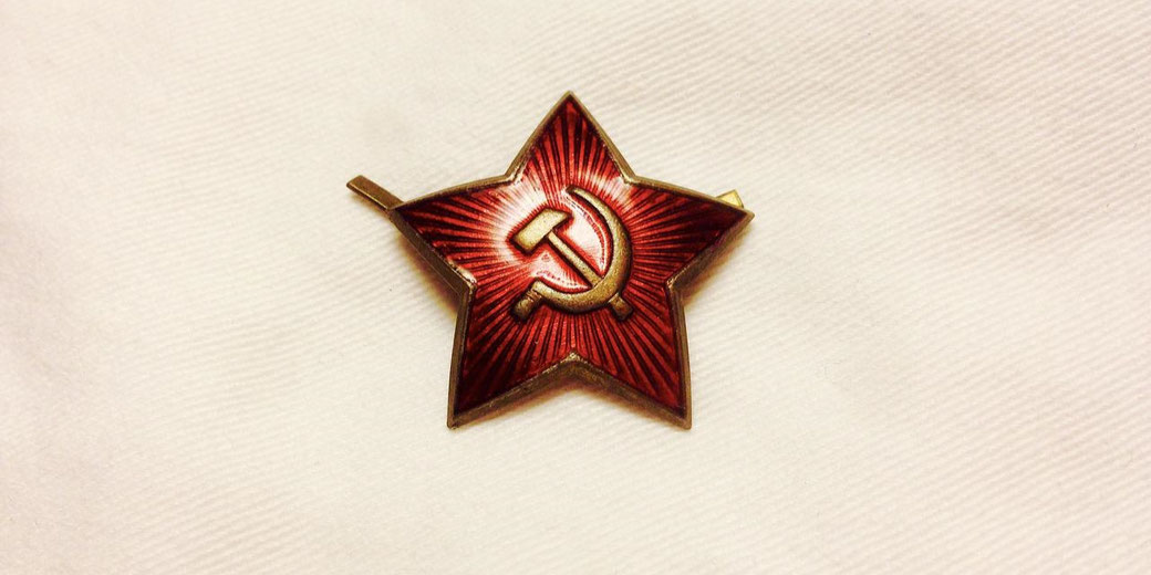 A Soviet Red Army cap badge featuring a red star with a gold hammer and sickle emblem, symbolizing communism. It rests on a white fabric background.