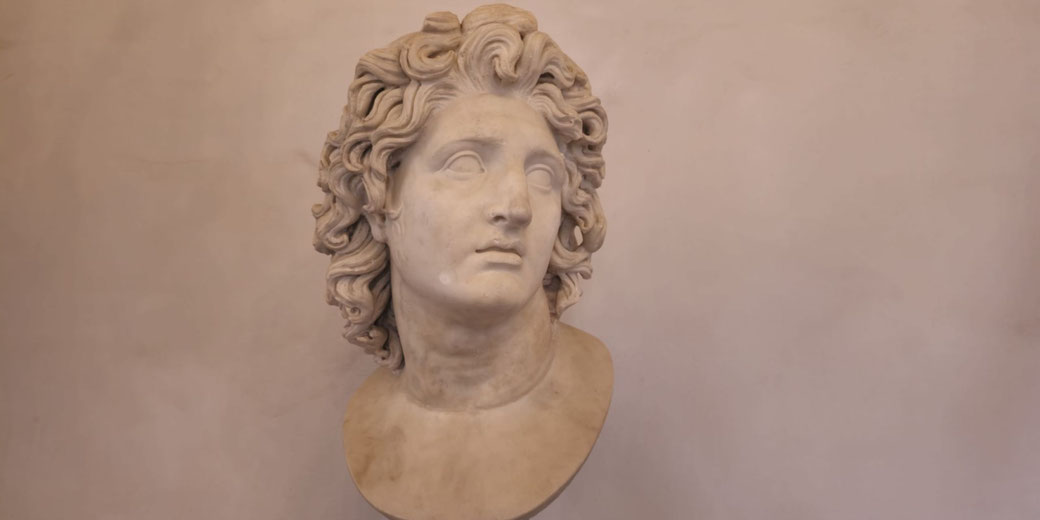 Marble bust of a youthful man with flowing curly hair, gazing slightly upward with a calm, idealized expression.