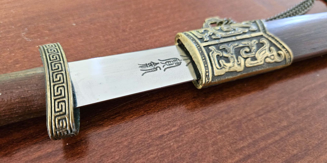 An ornate sword with a bronze hilt and scabbard featuring intricate patterns and engravings. The blade displays Chinese characters, blending artistry with functional design.