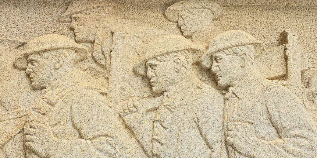 Stone relief sculpture depicting World War I soldiers marching in formation, wearing helmets and carrying gear.