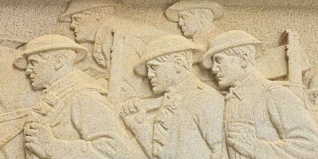 Stone relief sculpture depicting World War I soldiers marching in formation, wearing helmets and carrying gear.