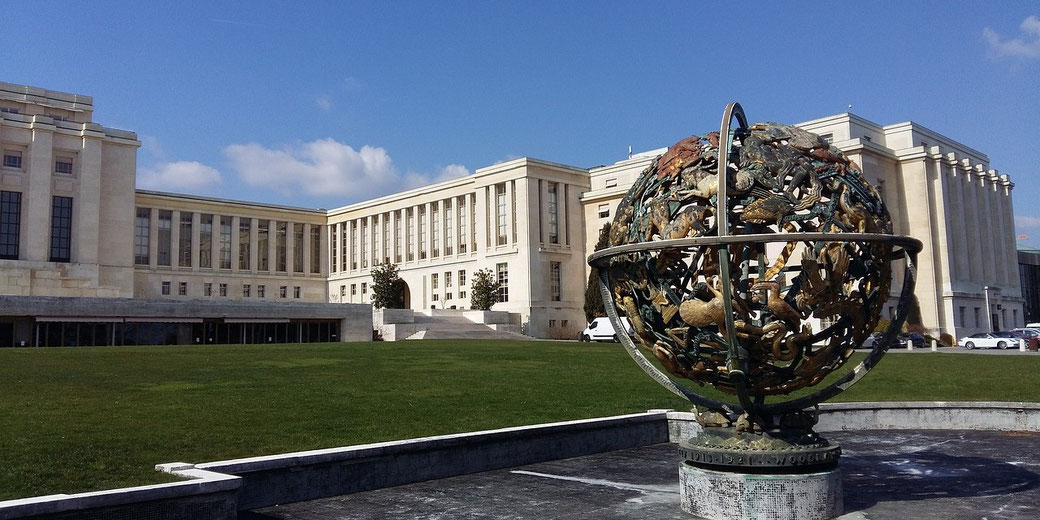 A bronze armillary sphere sculpture stands before the grand facade of the Palace of Nations in Geneva.