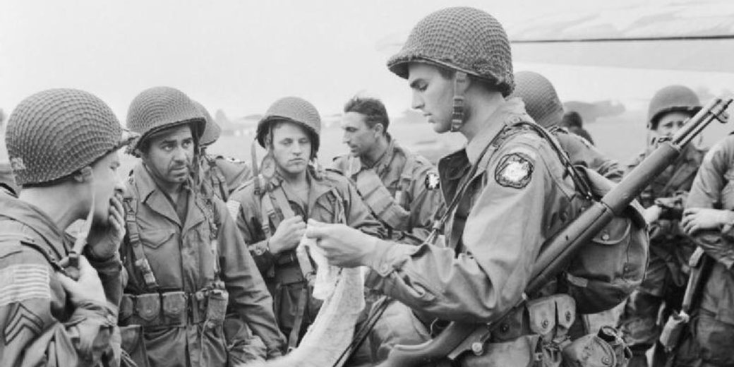 Group of paratroopers in uniform and helmets review a map or instructions before deployment during World War II.