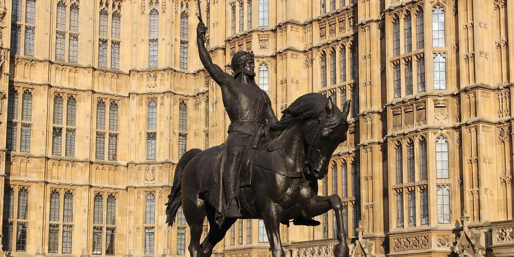 Equestrian statue of a warrior holding a sword raised high, set before a Gothic-style building with tall windows.