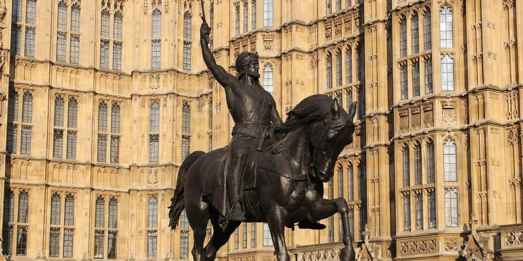 Equestrian statue of a warrior holding a sword raised high, set before a Gothic-style building with tall windows.