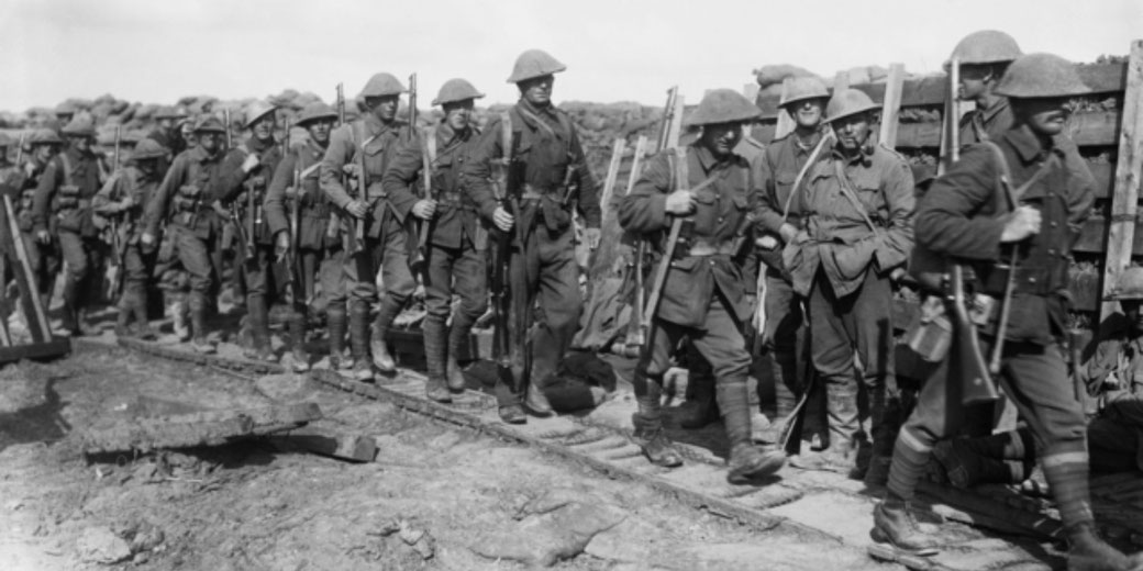 Australian soldiers march along a duckboard track toward front-line trenches in Northern France, with timber-reinforced breastworks and sandbags visible behind them.