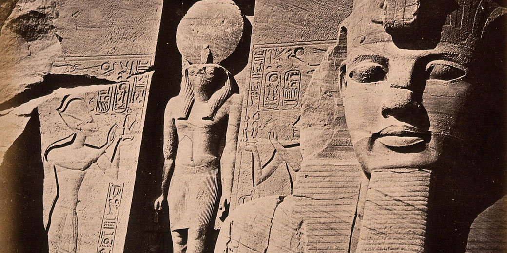 Close-up of ancient Egyptian stone carvings showing a pharaoh’s face, a sun-crowned deity, and surrounding hieroglyphic reliefs.