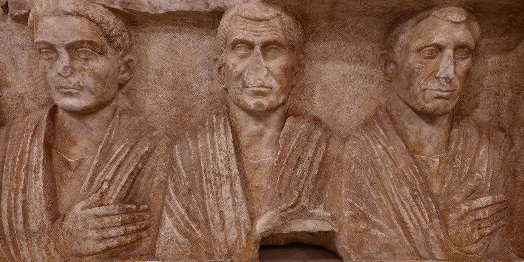 Stone relief of three Roman men in togas, shown from the chest up, with solemn expressions and crossed arms.