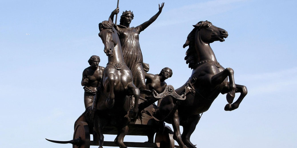 Bronze statue of a warrior queen in a chariot drawn by rearing horses, flanked by two figures, against a clear sky.