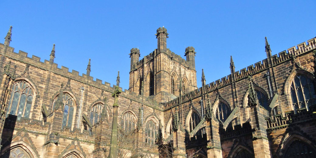 Chester Cathedral, a grand Gothic-style church in England. Originally a Benedictine abbey, it features intricate stonework, pointed arches, and towering spires against a clear blue sky.