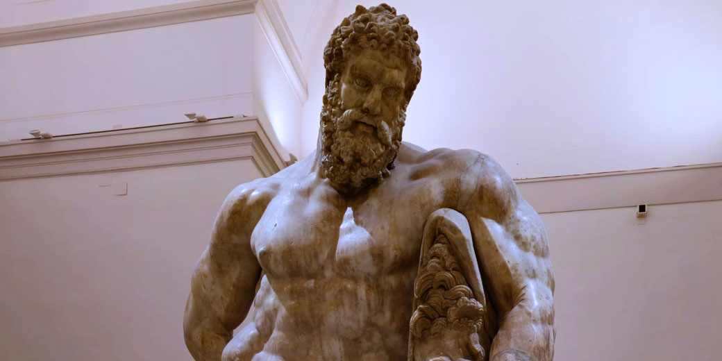 Massive marble statue of a bearded, muscular man looking down, holding a lion skin—symbol of strength, often associated with Hercules.