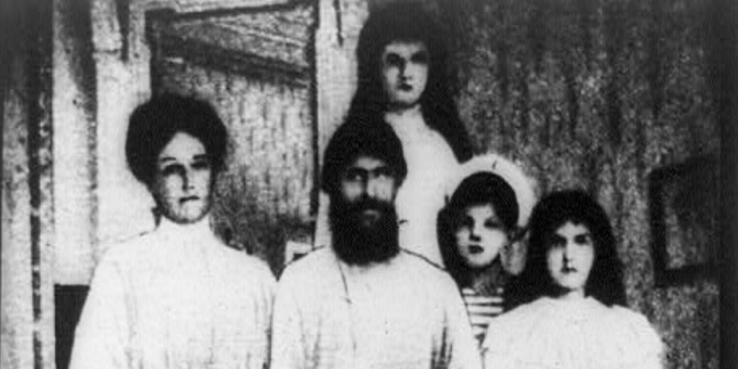 A bearded man stands with four young individuals in a dimly lit room, all facing the camera with serious expressions in a grainy black and white image.