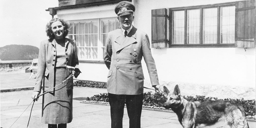 Black and white historical photograph of Adolf Hitler and Eva Braun with dogs at the Berghof.