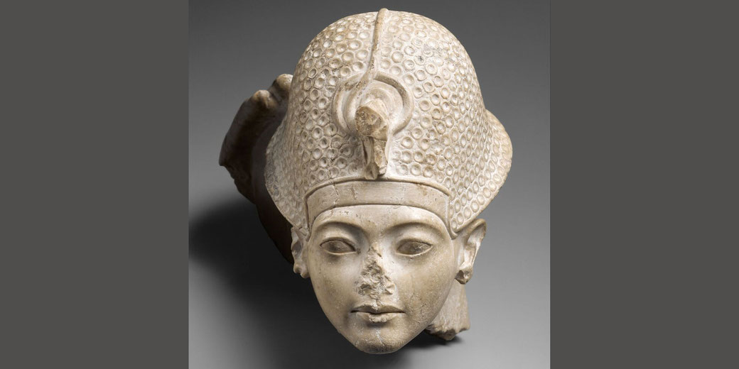 A sculpted head of Pharaoh Tutankhamun, wearing a detailed Nemes headdress with a uraeus cobra. The limestone carving features finely crafted facial details but has some damage to the nose.