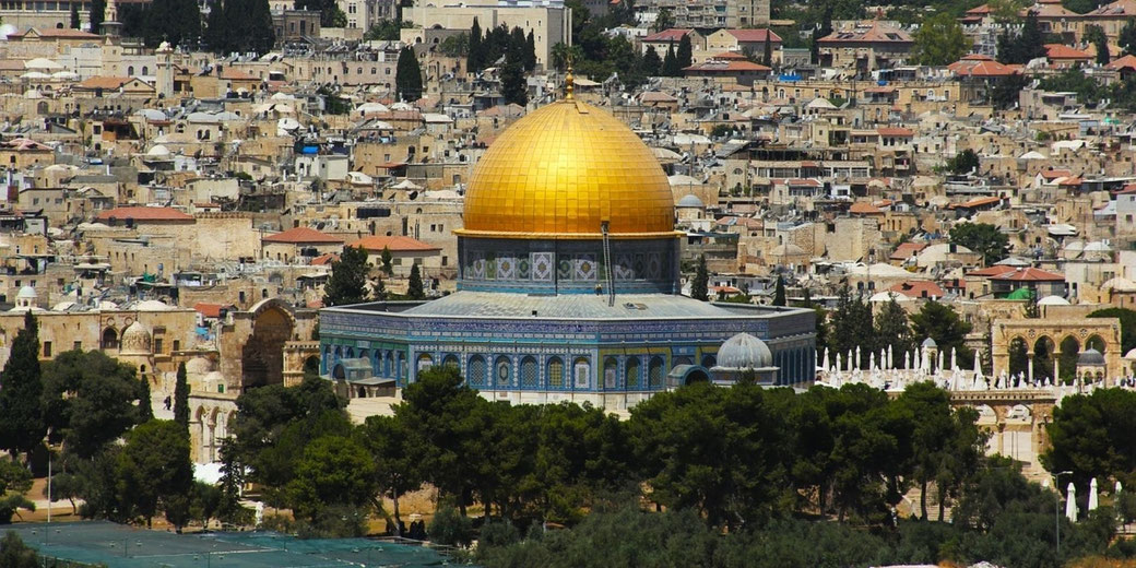 The Dome of the Rock in Jerusalem, with its golden dome and intricate blue tilework, surrounded by the city's historic buildings and greenery.