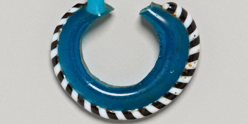A blue glass earring shaped by heating and bending around a rod. It is one half of a pair, showing early glassworking techniques from ancient Egypt.
