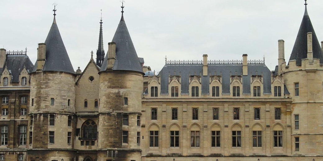 A grand historic building with medieval-style round towers, pointed roofs, and arched windows. The intricate detailing and stone facade suggest a castle or former palace.