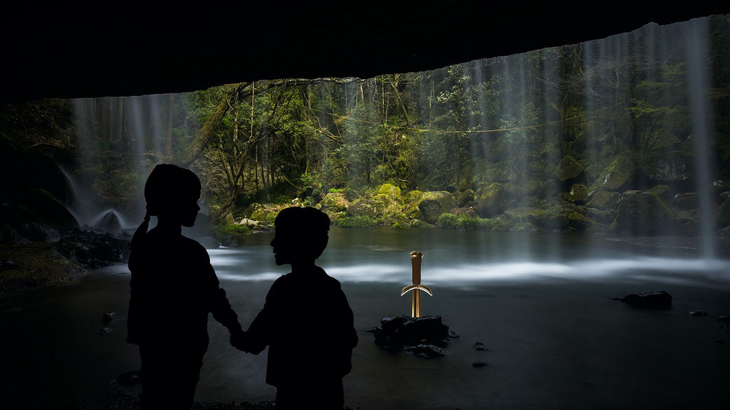 Two silhouetted children holding hands in a cave, gazing at a glowing sword embedded in a rock near a mystical waterfall.
