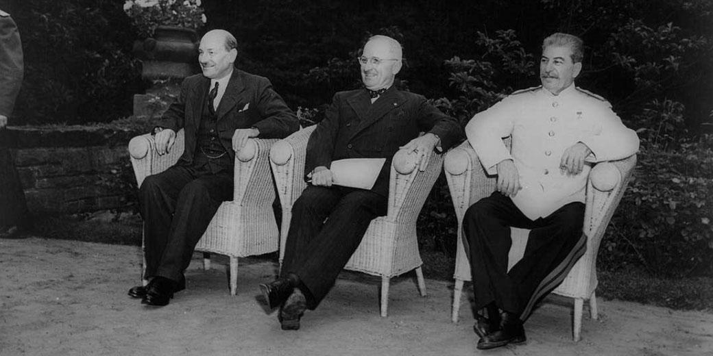 Three world leaders seated outdoors in wicker chairs during a wartime conference, dressed in formal attire, smiling as they pose for a historic photograph.