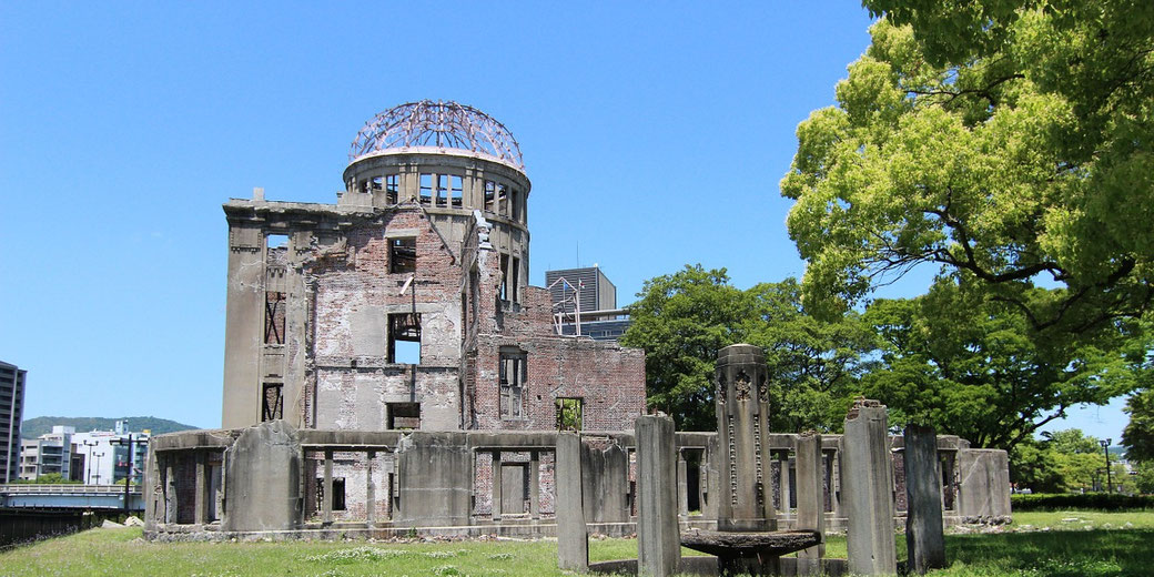 A ruined brick building with a skeletal dome stands surrounded by greenery under a clear sky, marking a historic wartime site.
