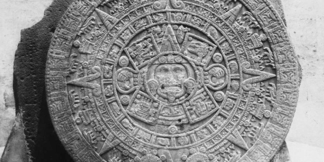The Aztec Sun Stone, also known as the Calendar Stone. It is a massive circular stone with intricate carvings representing Aztec cosmology, time cycles, and deities, including Tonatiuh at the center.