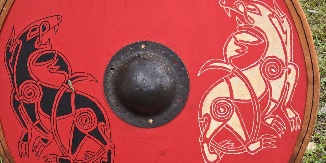 A round shield with a red background, featuring black and white stylized animal designs. A metal boss is at the center, and the rim is reinforced.