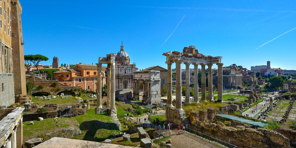 Panoramic view of the Roman Forum with ancient ruins, columns, and historic buildings under a clear blue sky.