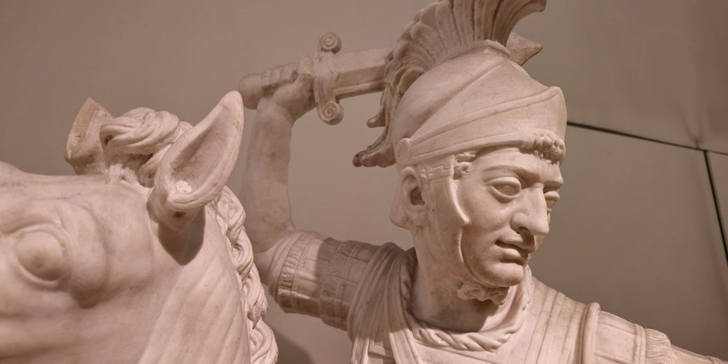 Detailed marble sculpture of a Roman soldier on horseback, raising a sword with a focused expression and wearing a plumed helmet.