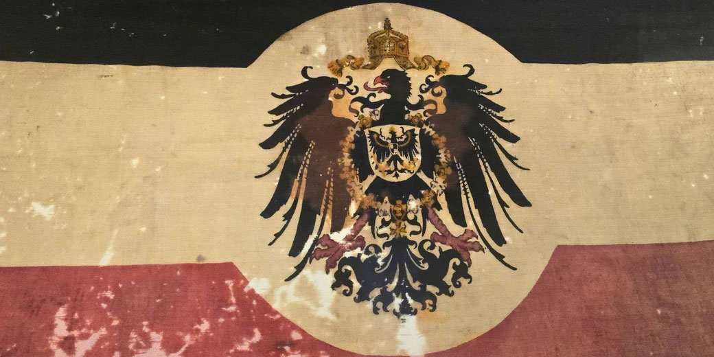 A historical German Empire flag featuring black, white, and red stripes with a crowned black eagle emblem in the center.