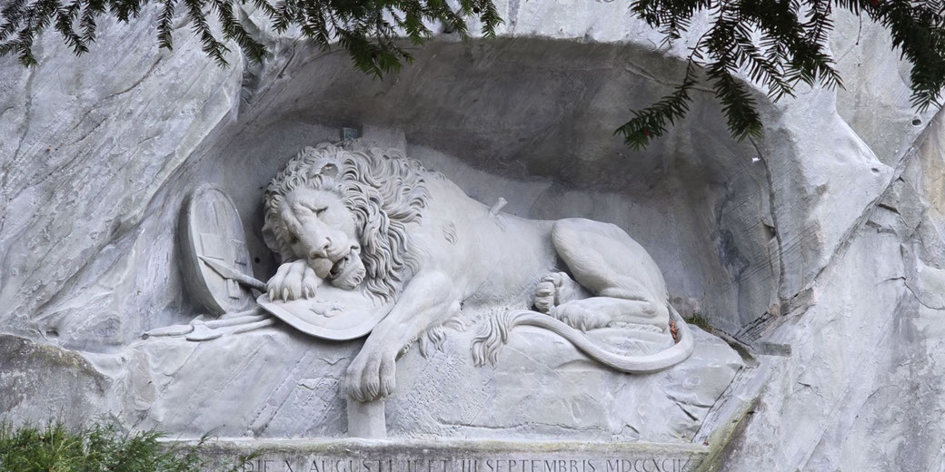 The Lion Monument in Lucerne, Switzerland, a carved stone sculpture of a dying lion resting on a shield with a spear in its side, commemorating fallen Swiss Guards. It’s set in a rocky niche.