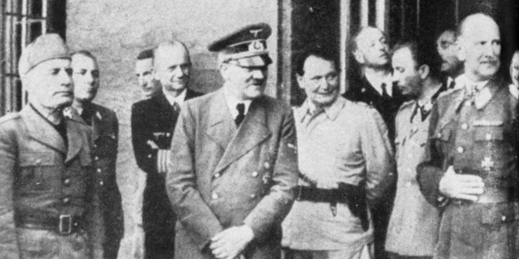Black-and-white photo of WWII-era military leaders in uniform standing together in a group, some smiling, in front of a building.
