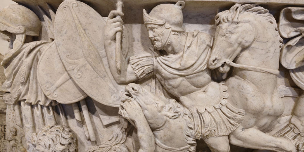 Marble relief of a Roman cavalryman raising a weapon, surrounded by shields and charging horses in a dynamic battle scene.