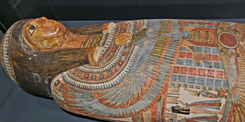 An ancient Egyptian sarcophagus adorned with intricate painted designs, including winged deities and hieroglyphs. The detailed face and vibrant colors highlight its craftsmanship and symbolism.