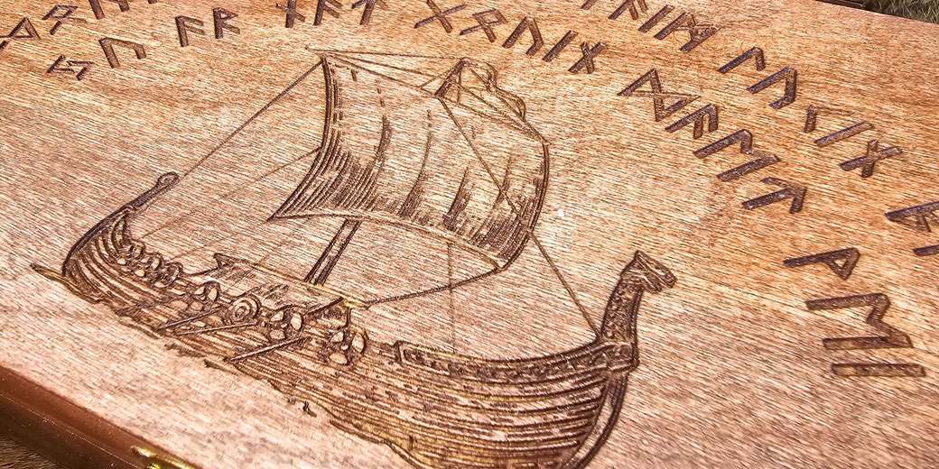 A wooden surface with an engraved Viking longship, featuring a sail and rowers.