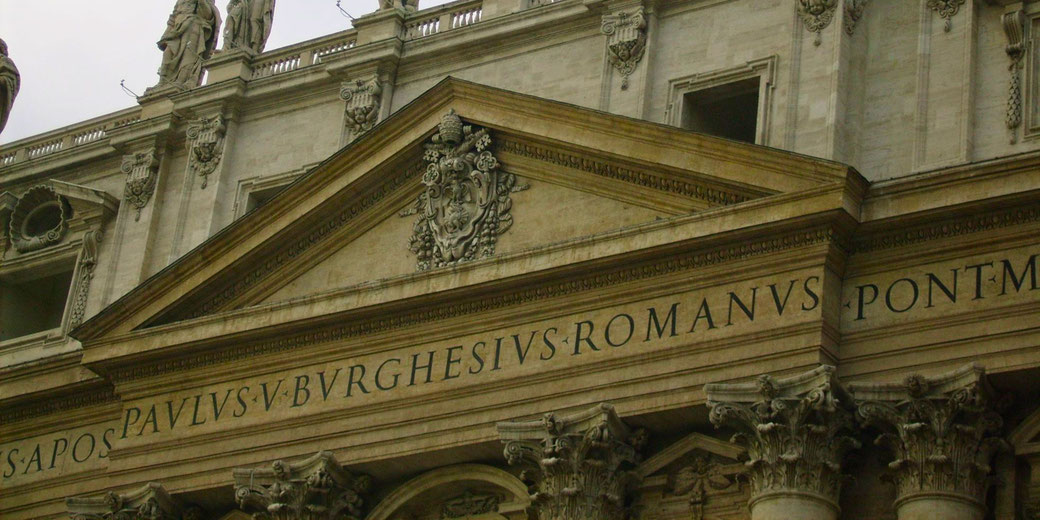 The façade of St. Peter's Basilica in Vatican City, featuring Latin inscriptions, Baroque architecture, and statues of saints adorning the upper level.