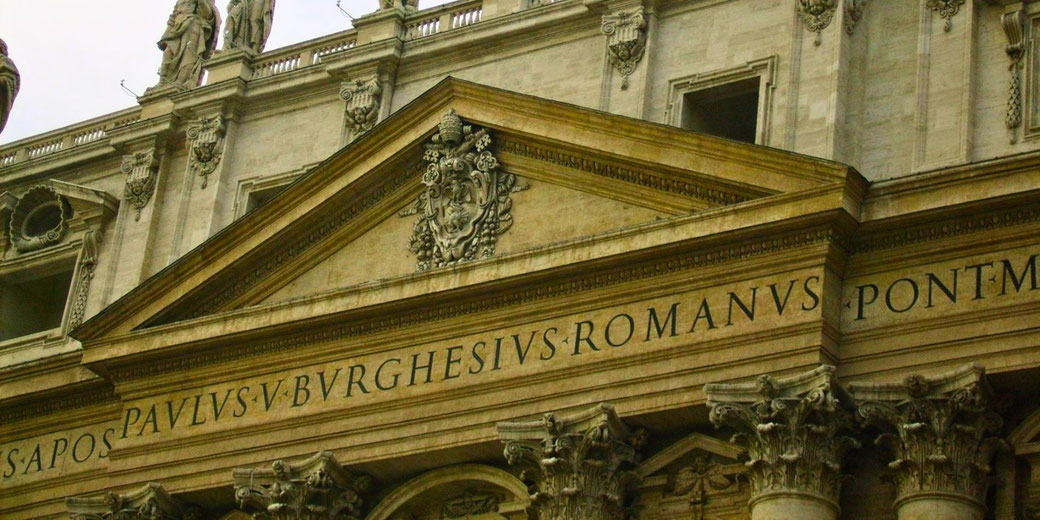 The façade of St. Peter's Basilica in Vatican City, featuring Latin inscriptions, Baroque architecture, and statues of saints adorning the upper level.