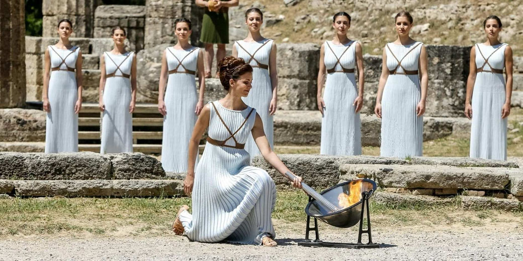 Women dressed as ancient Greek priestesses lighting the Olympic torch in a traditional ceremony at Olympia.