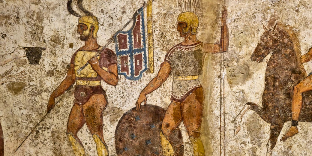 Ancient fresco depicts armored warriors with helmets, shields, and spears, one carrying a decorated standard; a horse and rider appear on the right side.