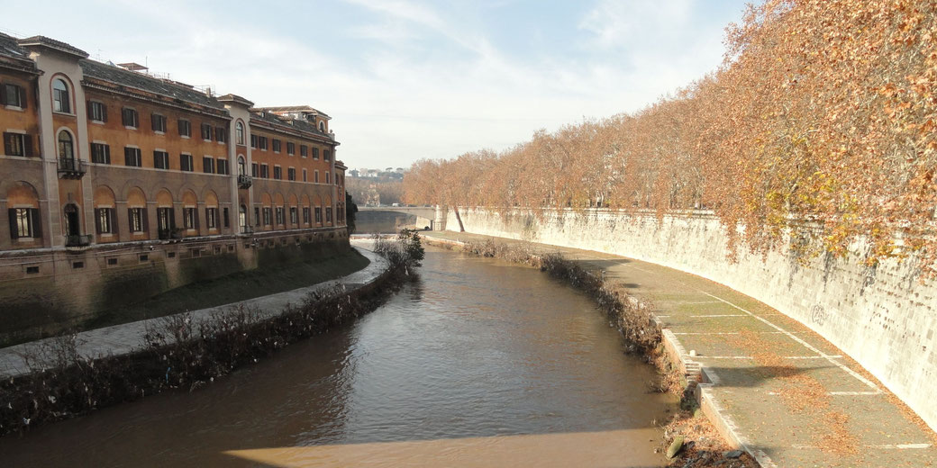 Curving river with autumn trees and a historic building lining its banks under a clear sky.