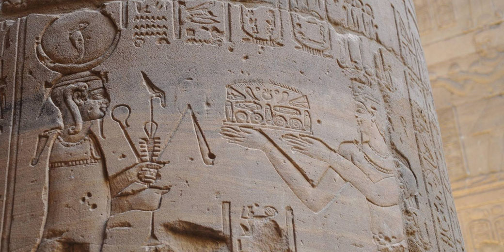 Ancient Egyptian relief carved into a stone temple wall, with hieroglyphs and two figures in profile holding ceremonial objects and offerings.