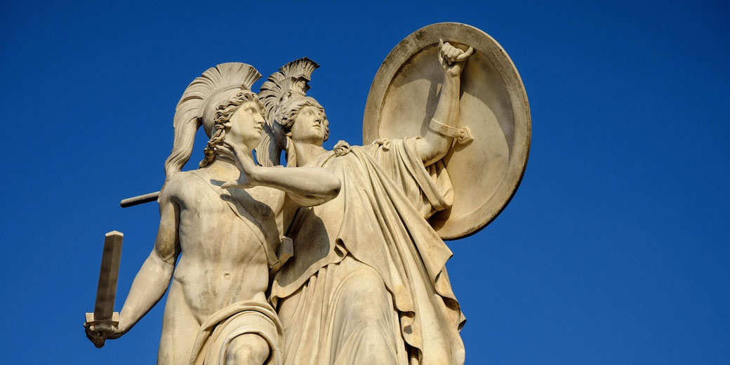 A marble statue of an ancient Greek warrior, sword in hand, alongside Athena, who raises a shield.